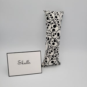 May include: A white pillow with a black skull pattern. The pillow is rectangular and has a label that says "Skulls".