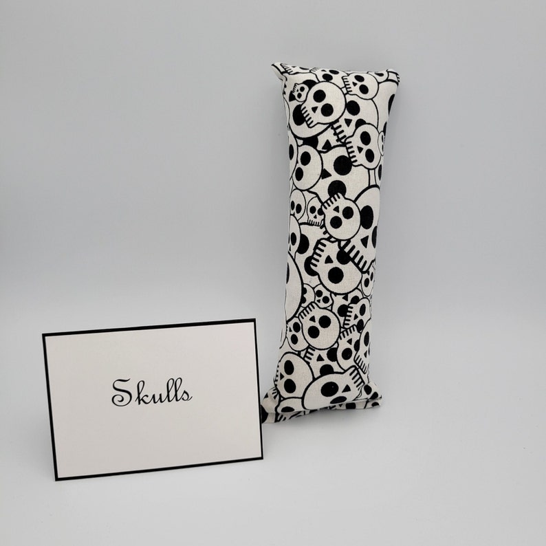 May include: A white pillow with a black skull pattern. The pillow is rectangular and has a label that says "Skulls".