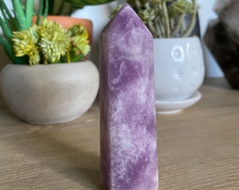 May include: A purple amethyst crystal point with a smooth, polished surface. The crystal is shaped like a tall, slender pyramid.