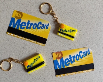 Puede incluir: Se muestran varias réplicas amarillas de MetroCard, algunas como llaveros. Las tarjetas muestran el logotipo de la MTA y la palabra "MetroCard" en azul. También es visible el texto "Insert this way / This side facing you". Los llaveros tienen anillos dorados.