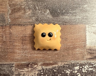 Puede incluir: Un ravioli amarillo hecho a mano con una cara sonriente y ojos negros.
