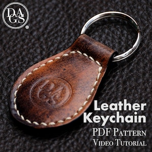 Puede incluir: Un llavero de cuero marrón con detalles de costura blanca y un anillo de llave plateado. El llavero tiene un logotipo circular en relieve en la parte delantera. El texto "Leather Keychain" está impreso en blanco sobre fondo negro, con las palabras "PDF PATTERN" y "VIDEO TUTORIAL" impresas debajo.