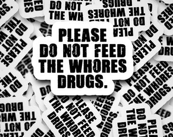 May include: A collection of white stickers with black text. The primary sticker reads "PLEASE DO NOT FEED THE WHORES DRUGS." Other stickers repeat the same phrase. The stickers are scattered across a surface.
