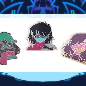 May include: Three enamel pins featuring characters from the video game Deltarune. The pins are of Kris, Susie, and Ralsei. Kris is a human with black hair and a blue eye patch. Susie is a purple-haired monster with sharp teeth. Ralsei is a green-haired monster with a red scarf and glasses.