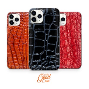 Puede incluir: Tres fundas para iPhone con un patrón de piel de cocodrilo. Las fundas son de color negro, rojo y marrón.