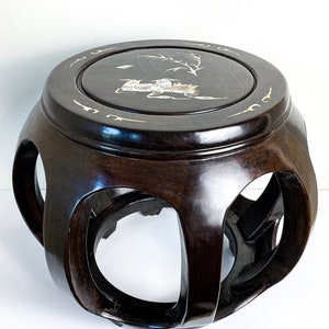 May include: A dark brown wooden stool with a round top and a carved design. The top is inlaid with mother-of-pearl and features a floral motif.