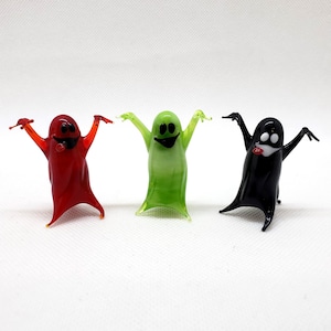 以下が含まれることがあります： 笑顔の顔をしたガラス製の幽霊の置物3つ。幽霊は赤、緑、黒です。