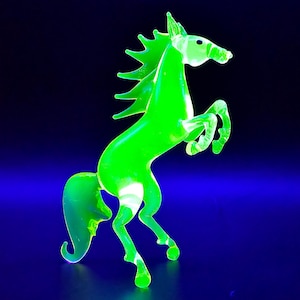 May include: A neon green glass horse figurine rearing up on its hind legs. The horse has a flowing mane and tail, and is set against a dark blue background. The figurine is approximately 6 inches tall.