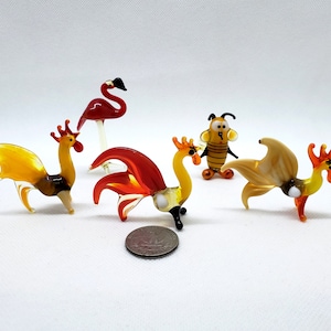 Pode incluir: Cinco estatuetas de animais de vidro, incluindo um flamingo, uma abelha e três galos. Os galos são de várias cores, incluindo amarelo, laranja e vermelho. As estatuetas são todas pequenas e seriam perfeitas para uma coleção em miniatura.