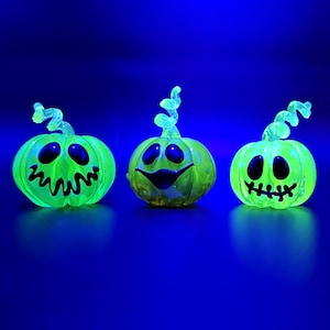 以下が含まれることがあります： 黒い顔とカールした茎を持つ、3つの光る緑色のハロウィーンカボチャの装飾。 カボチャは暗い青色の背景に照らされており、不気味でフェスティバルな雰囲気を作り出しています。 ハロウィーンに最適です。