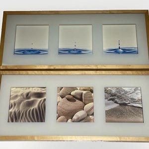 May include: Two rectangular wall frames with light wood finish, each containing three square prints. The top frame displays blue water droplet ripples. The bottom frame features a sand dune, a pile of smooth brown stones, and ocean waves.