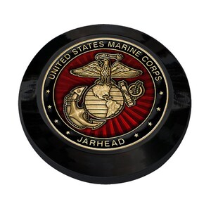 May include: A black and gold round emblem with the United States Marine Corps logo. The logo features a globe with an eagle perched on top and an anchor below. The text "United States Marine Corps" is written in a circle around the logo. The text "Jarhead" is written below the logo.