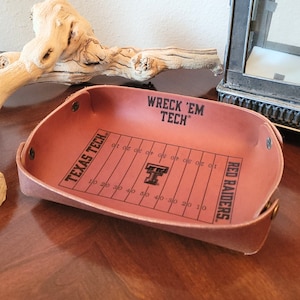 May include: A brown leather tray with a football field design and the words "Wreck 'Em Tech" and "Red Raiders" printed on it. The tray also has the Texas Tech logo in the center.