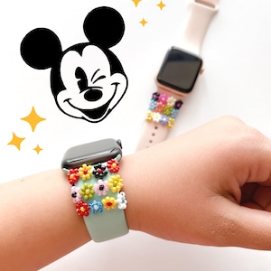 Puede incluir: Una banda de Apple Watch azul claro con un diseño de flores de cuentas de colores. La banda está en la muñeca de una persona.