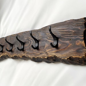 May include: A rustic wooden coat rack with a natural, dark brown finish. The rack has five black metal hooks and a rough, uneven edge.