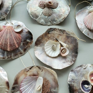 May include: A set of nine decorative ornaments made from seashells. Each ornament features a different arrangement of seashells, including scallop shells, cockle shells, and other small shells. The ornaments are attached to a string and can be hung on a Christmas tree or used as a decorative element in a home.