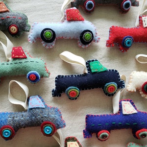 May include: A collection of felt truck ornaments in various colors, including red, blue, green, and gray. Each truck has a different colored cab and a white felt bed. The trucks have felt wheels with colorful buttons for details.