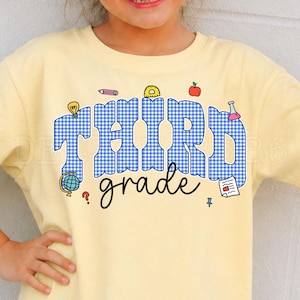 Könnte beinhalten: Ein hellgelbes T-Shirt mit dem Text THIRD in blau-weißem Vichy-Muster und dem Wort grade in schwarzer Schreibschrift. Das Design enthält kleine bunte Illustrationen eines Bleistifts, eines Geodreiecks, eines Apfels, einer Glühbirne und eines Globus.