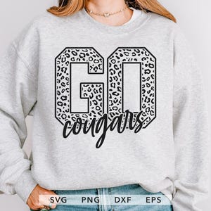 May include: A pale grey sweatshirt featuring the text "GO Cougars" in black. The letters "GO" are filled with a leopard print design. The word "cougars" is written in a cursive font.