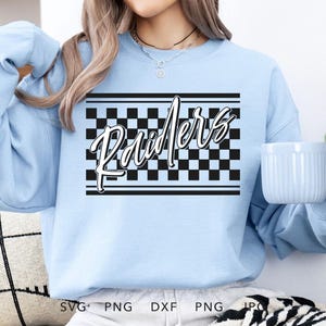 Puede incluir: Sudadera azul claro con un patrón de cuadros negros y blancos y la palabra "Raiders" en letras blancas cursivas.