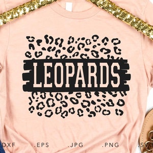 Puede incluir: Una camiseta rosa con un diseño de estampado de leopardo negro y la palabra "LEOPARDS" en letras blancas sobre un fondo negro.