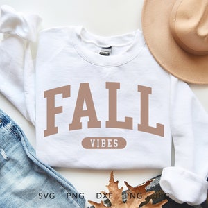 May include: White sweatshirt with the words "FALL VIBES" in brown block letters. The sweatshirt is laid on top of blue jeans, with a coffee cup and a tan hat in the background. The image also includes SVG, PNG, DXF, and JPG file type icons.