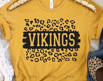 May include: A mustard yellow t-shirt with a black and white leopard print design. The word "VIKINGS" is written in black letters with a yellow outline on a black rectangle.