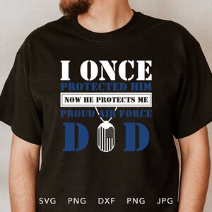 May include: Black t-shirt with white text that reads "I once protected him now he protects me proud air force DOD". The text is surrounded by a blue and white American flag design.