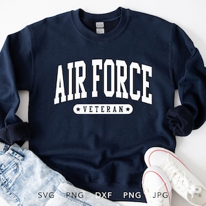 May include: Navy blue sweatshirt with the text "AIR FORCE VETERAN" in white block letters. The sweatshirt is paired with light-wash denim jeans and white sneakers.