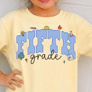 May include: A pale yellow t-shirt featuring the text FIFTH in large blue and white gingham letters and the word grade in black cursive script. The design includes small colorful school-themed icons like a globe, pencil, apple, and beaker.