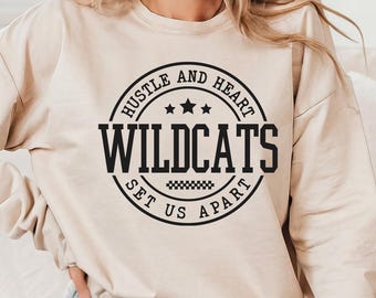 May include: A beige sweatshirt with a black circular graphic that reads "Hustle and Heart Wildcats Set Us Apart." The graphic includes stars and a checkered pattern. The bottom of the image shows the file types: SVG, PNG, DXF, and EPS.