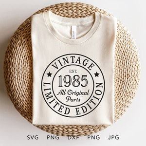 May include: A cream-colored t-shirt with a black circular graphic that reads "VINTAGE EST. 1985 LIMITED EDITION All Original Parts." The shirt is laid on a woven, circular surface. The bottom of the image shows file type abbreviations.