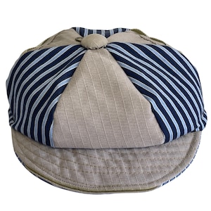May include: A newsboy cap in beige and navy blue stripes. The cap has a rounded crown and a short, curved peak. The crown is divided into panels, with a button detail at the top.