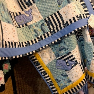 May include: A blue and white baby quilt with a whale pattern. The quilt is made of patchwork fabric and has a blue and white striped border.