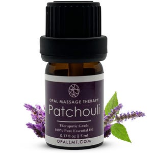 May include: A small brown glass bottle with a black cap, labeled "OPAL MASSAGE THERAPY Patchouli Therapeutic Grade 100% Pure Essential Oil 0.17 fl oz | 5 ml OPALLMT.COM". The bottle is surrounded by green and purple foliage.