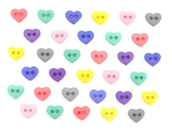 May include: A selection of heart-shaped buttons in a range of colours: red, green, blue, yellow, pink, purple, and grey. Each button has two holes for sewing. The buttons are arranged on a white background.