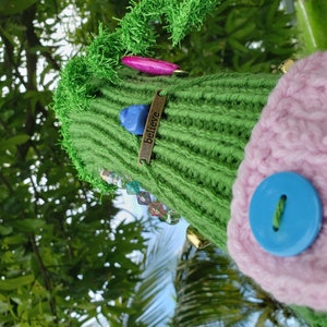 May include: A green knitted Christmas tree ornament with a pink and gold ribbon, a blue gem, and a gold tag that says "Believe".