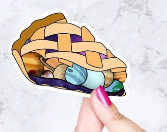 May include: A sticker of a pie crust filled with planets and stars. The pie crust is yellow and the planets are blue, green, and purple.