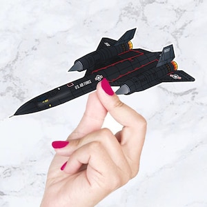 May include: A black and red SR-71 Blackbird jet plane sticker with the words "U.S. AIR FORCE" and "00327" printed on it.
