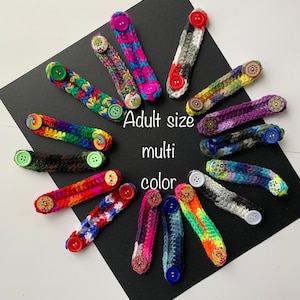May include: A collection of colorful crocheted mask extenders with buttons. The extenders are adult size and come in a variety of colors. The text "Adult size multi color" is written on a black background.