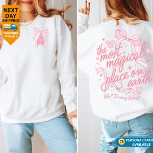 May include: White sweatshirt with a pink castle and bow design on the front. The back features the text "the most magical place on earth" with a bow and heart accents. Walt Disney World is printed below.