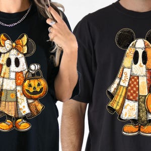 May include: Black t-shirts with a cartoon ghost character wearing Mickey Mouse ears and a patchwork quilt costume. The ghost is holding a jack-o'-lantern. The design features orange, yellow, and brown colours.