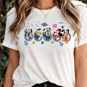 Pu&ograve; includere: T-shirt bianca con un design a tema nautico con Topolino, Pippo, Paperino, Topolino, Minnie e Pluto in obl&ograve;. Il design include ancore, stelle e un timone.