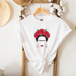 May include: White t-shirt with a black and white illustration of Frida Kahlo wearing a red flower crown.