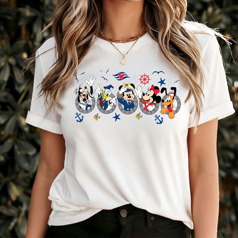 Pu&ograve; includere: T-shirt bianca con un design a tema nautico con Topolino, Pippo, Paperino, Topolino, Minnie e Pluto in obl&ograve;. Il design include ancore, stelle e un timone.