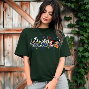 Pu&ograve; includere: T-shirt verde scuro con un design a tema nautico con personaggi dei cartoni animati. Il design include Topolino, Minnie, Paperino e Pippo in tenute da marinai. La maglietta ha un girocollo e maniche corte.