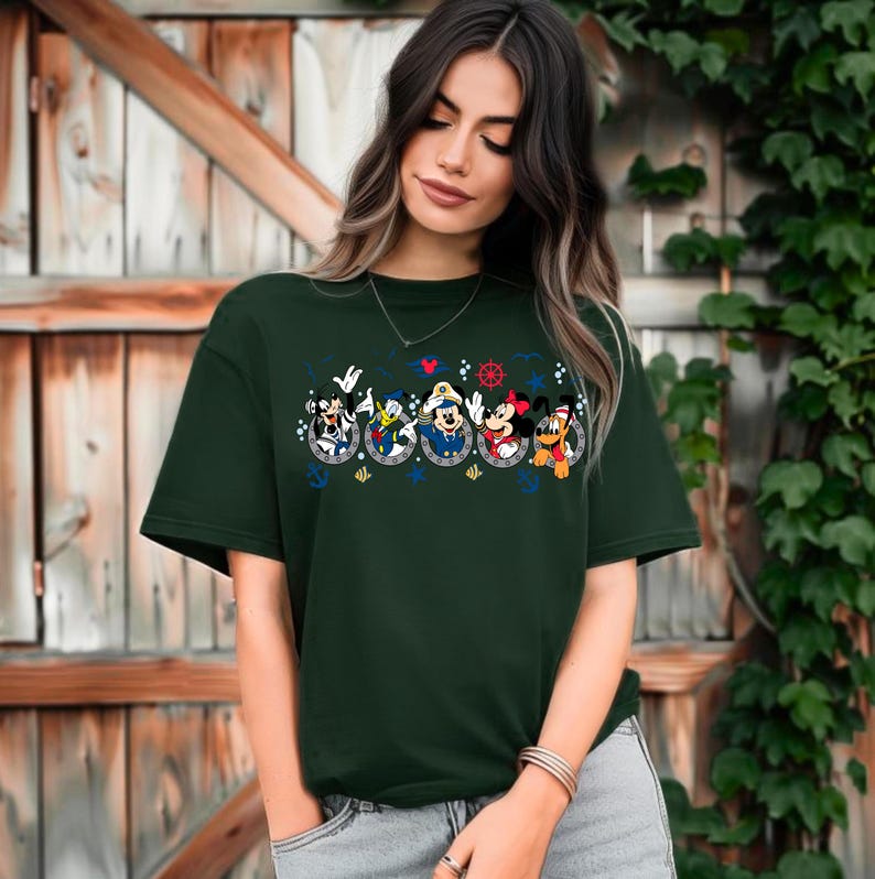 Pu&ograve; includere: T-shirt verde scuro con un design a tema nautico con personaggi dei cartoni animati. Il design include Topolino, Minnie, Paperino e Pippo in tenute da marinai. La maglietta ha un girocollo e maniche corte.