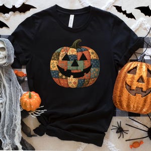 May include: Black t-shirt with a patchwork pumpkin design and a smiling face. The image is decorated with Halloween-themed items, including pumpkins, bats, spiders, and a skeleton.