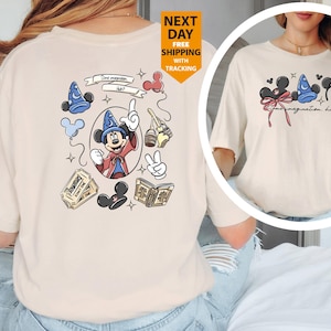 May include: Cream-colored t-shirt featuring a Mickey Mouse graphic. The design includes Mickey Mouse in a sorcerer's hat, along with other Disney-themed elements. The text "Some imagination, huh?" is also present.