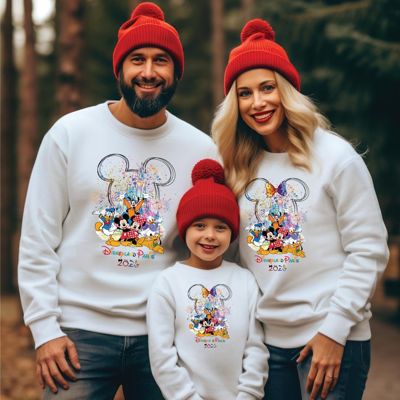May include: White sweatshirts featuring a Mickey Mouse design and the text "Disney in Paris 2024". The sweatshirts are paired with red bobble hats. The design includes Disney characters and a castle.